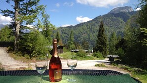 Une bouteille de Martini sur une table, accompagnée de deux verres, le tout sur fond de paysage montagneux.