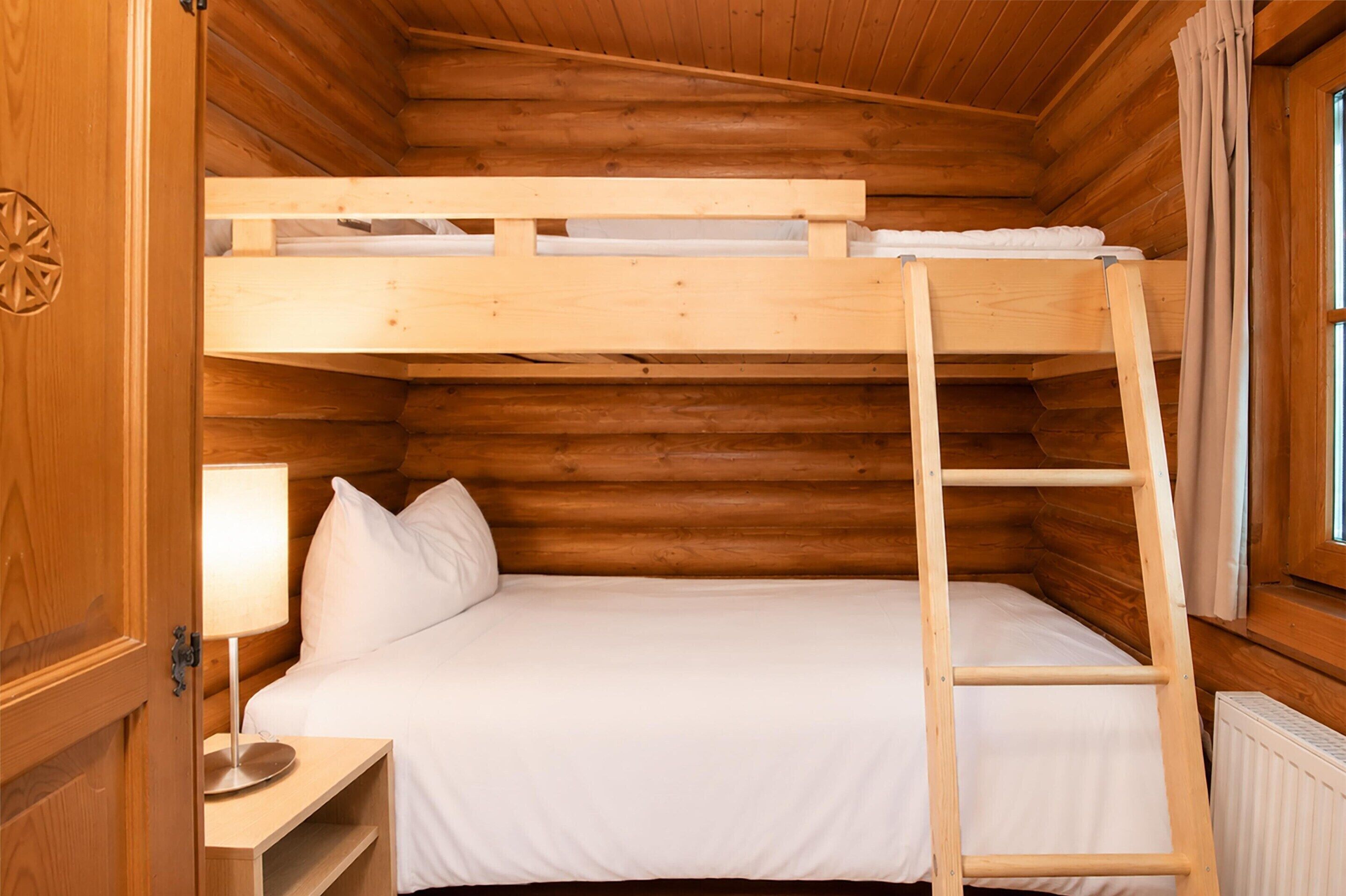 A bunk bed with a ladder, a bedside table with a lamp, and a window with curtains.