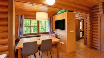 Un interior de madera con una zona de comedor, un televisor y un ventanal con cortinas.