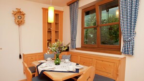 A dining area with a wooden table, blue cushioned chairs, a vase with flowers, and a window with checkered curtains. - Sunlit Apartment near Ski Area in Mittersill (Mittersill)