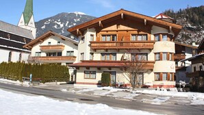 Un hôtel à plusieurs étages, de style architectural alpin traditionnel, doté de balcons et dont l’arrière-plan est dominé par un clocher d’église imposant.