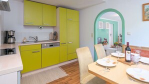 A bright kitchen with green cabinets, a dining table set for two, and a small dining area with a green archway. - Apartment With Mountain View (Piesendorf)