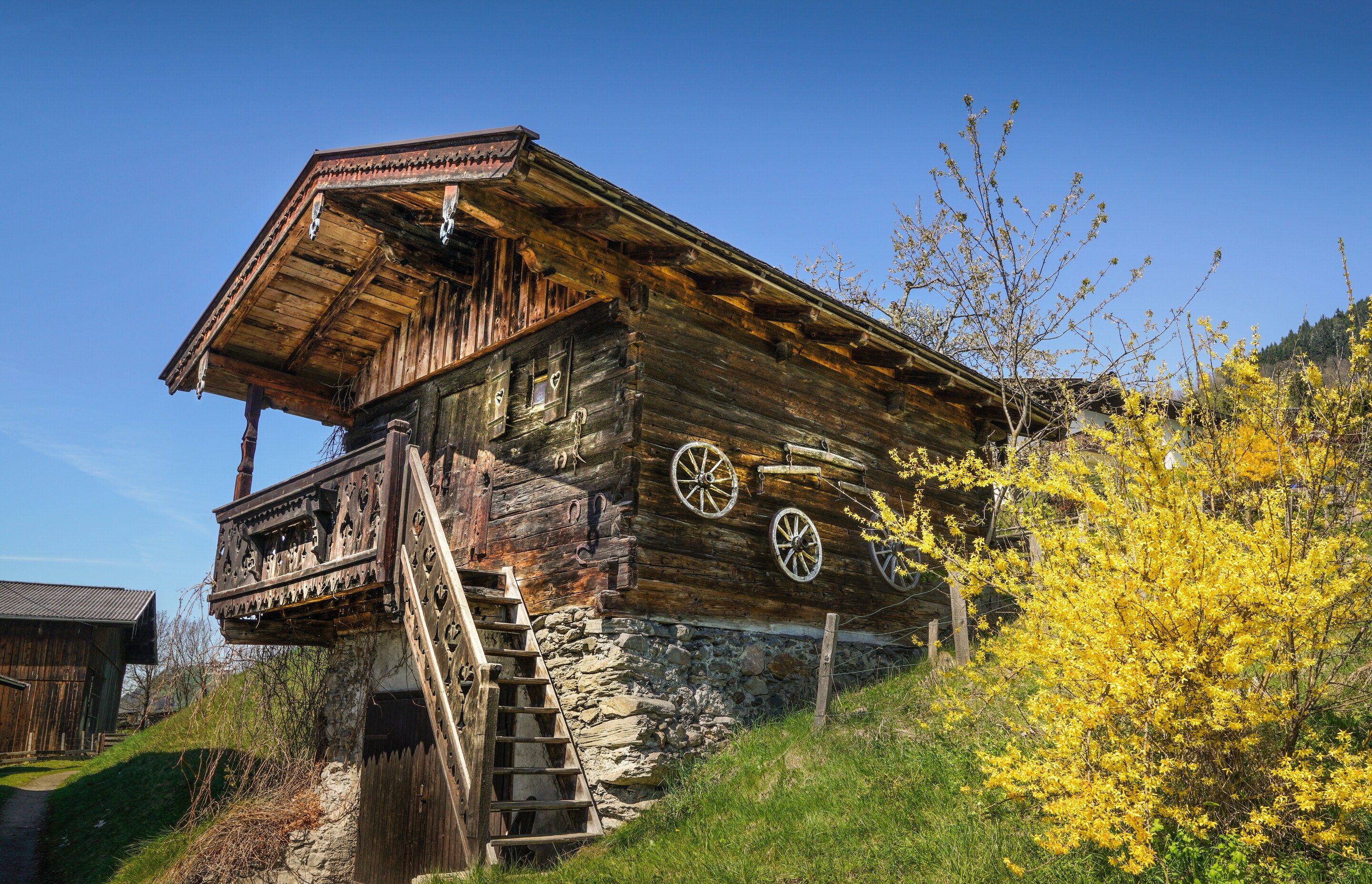 Ein rustikales Holzhaus mit Stein Fundament, einer Holztreppe, die zu einem Balkon führt, und einem Holzzaun, der das Grundstück umgibt.