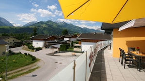 A terrace with a yellow umbrella, overlooking a mountain landscape and a village with traditional houses. - Chalet in Furth Near Zell am See Ski Slopes (Piesendorf)