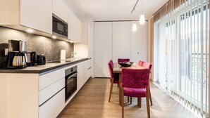 Cocina moderna con microondas, cafetera y horno integrados. Zona de comedor con mesa de madera y sillas rojas.