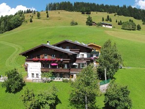 A large, multi-story chalet with a balcony and outdoor seating area, surrounded by lush green fields and trees. - Modern Holiday Home Near the ski Area (Maria Alm am Steinernen Meer)