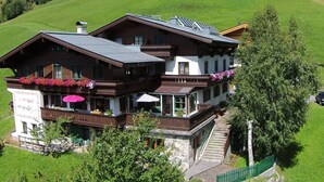 Een terras chalet met twee verdiepingen, omringd door weelderige groene heuvels.