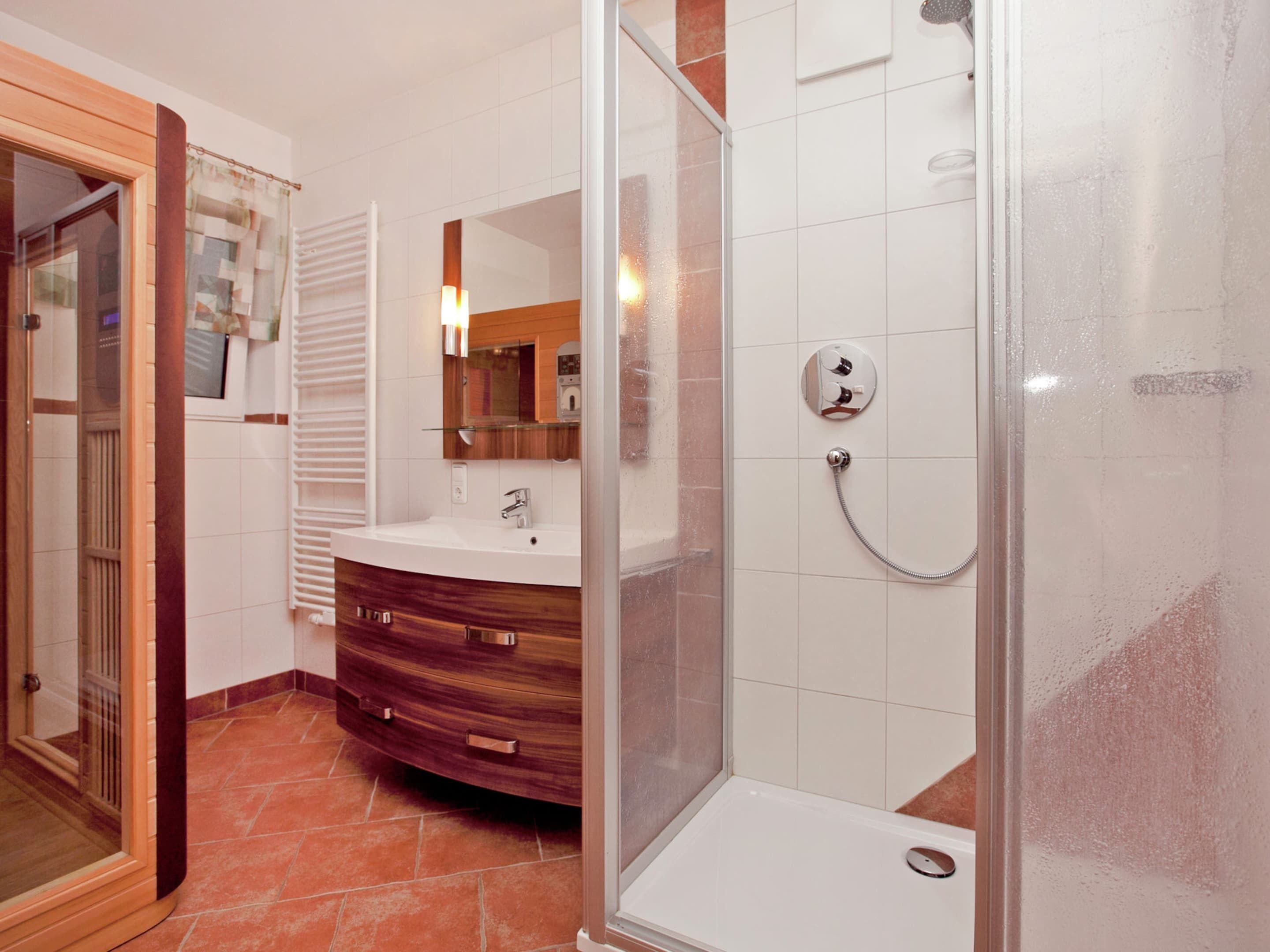 A modern bathroom with a glass shower enclosure, a vanity with a mirror, and a tiled floor.