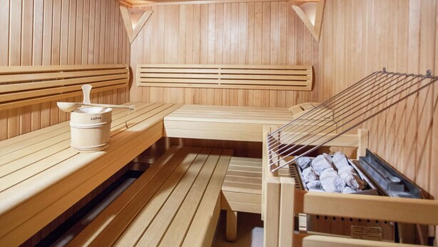 A sauna with wooden benches, a bench with a towel rack, and a sauna heater. - Apartment in Kaltenbach Near Ski Lift (Stumm)