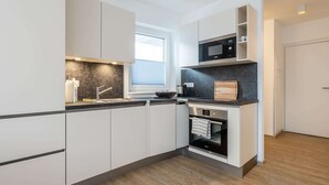 Een moderne keuken met witte kasten, een ingebouwde magnetron, een fornuis en een raam dat natuurlijk licht binnenlaat.