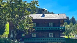 A two-story wooden house with a balcony, surrounded by greenery and trees. - Cozy Chalet in Bramberg am Wildkogel with Sauna near Ski Lift (Bramberg am Wildkogel)
