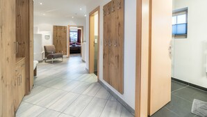 Un pasillo moderno de hotel con paneles de madera, una zona de estar con una silla y vistas a un dormitorio.