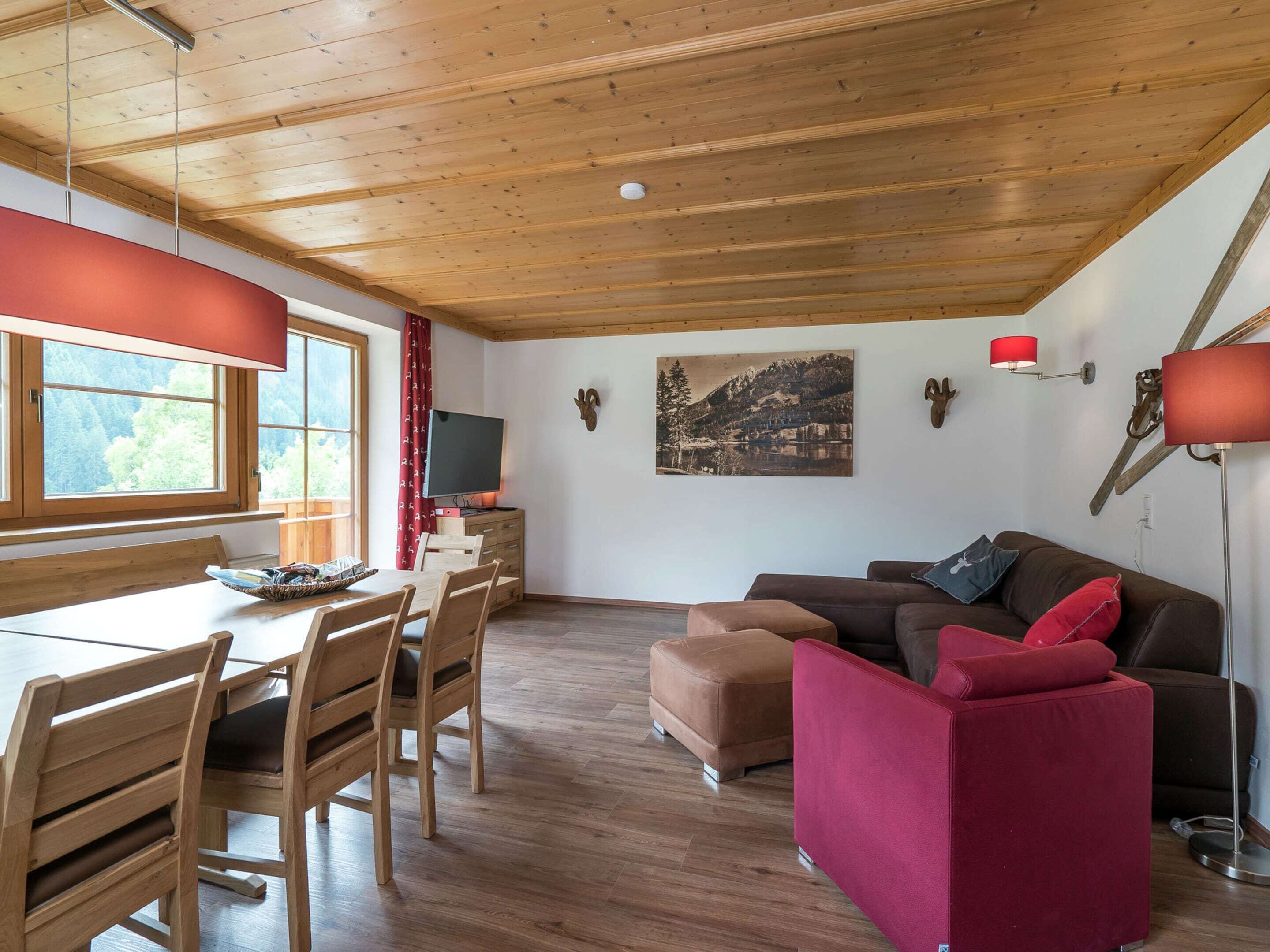 A cozy room with a wooden ceiling, a dining table with chairs, a sofa, and a mounted television.
