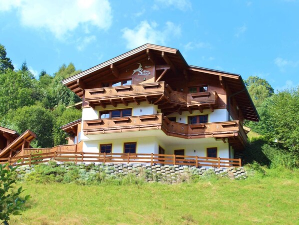 A multi-story chalet with wooden balconies and a stone foundation, surrounded by lush greenery.