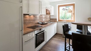 Ett modernt kök med vita skåp, en bänkskiva i trä, en inbyggd ugn och ett fönster med utsikt över grönområden.