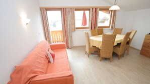 A room with a sofa, a dining table with chairs, a wooden bench, and a window with curtains.