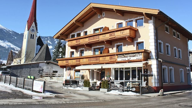 A multi-story building with a traditional Alpine architectural style, featuring a prominent clock tower and a balcony.