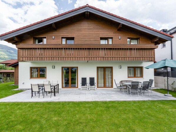 Une maison en bois à deux étages, dotée d’un balcon, d’une terrasse avec mobilier d’extérieur et offrant une vue sur le paysage environnant.