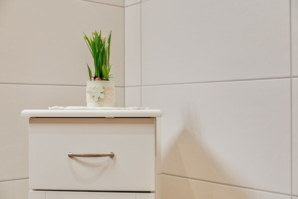 A bathroom with a white cabinet, a small potted plant, and white tiled walls.