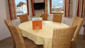 Una mesa redonda con mantel blanco y sillas de mimbre, un letrero con la marca 'Belvilla' y un televisor montado en la pared.