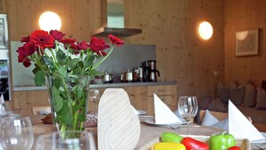 Una mesa de comedor con un florero de flores rojas, una cesta de verduras y copas de vino.