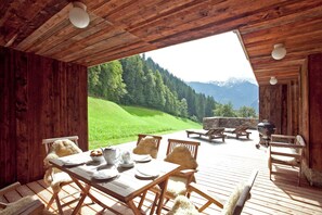 A wooden deck with a table set for dining, overlooking a green hillside and mountains. - Apartment in Ramsau Near Ski Bus (Ramsau im Zillertal)