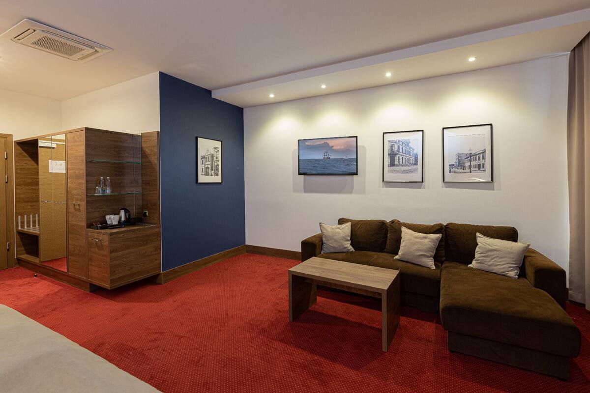 A hotel room with a wooden wardrobe, a red carpet, a brown sofa, and three framed pictures on the wall.