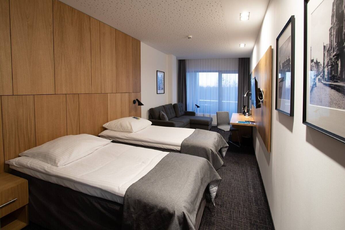 A hotel room with two beds, a desk, a chair, and a large window with curtains.
