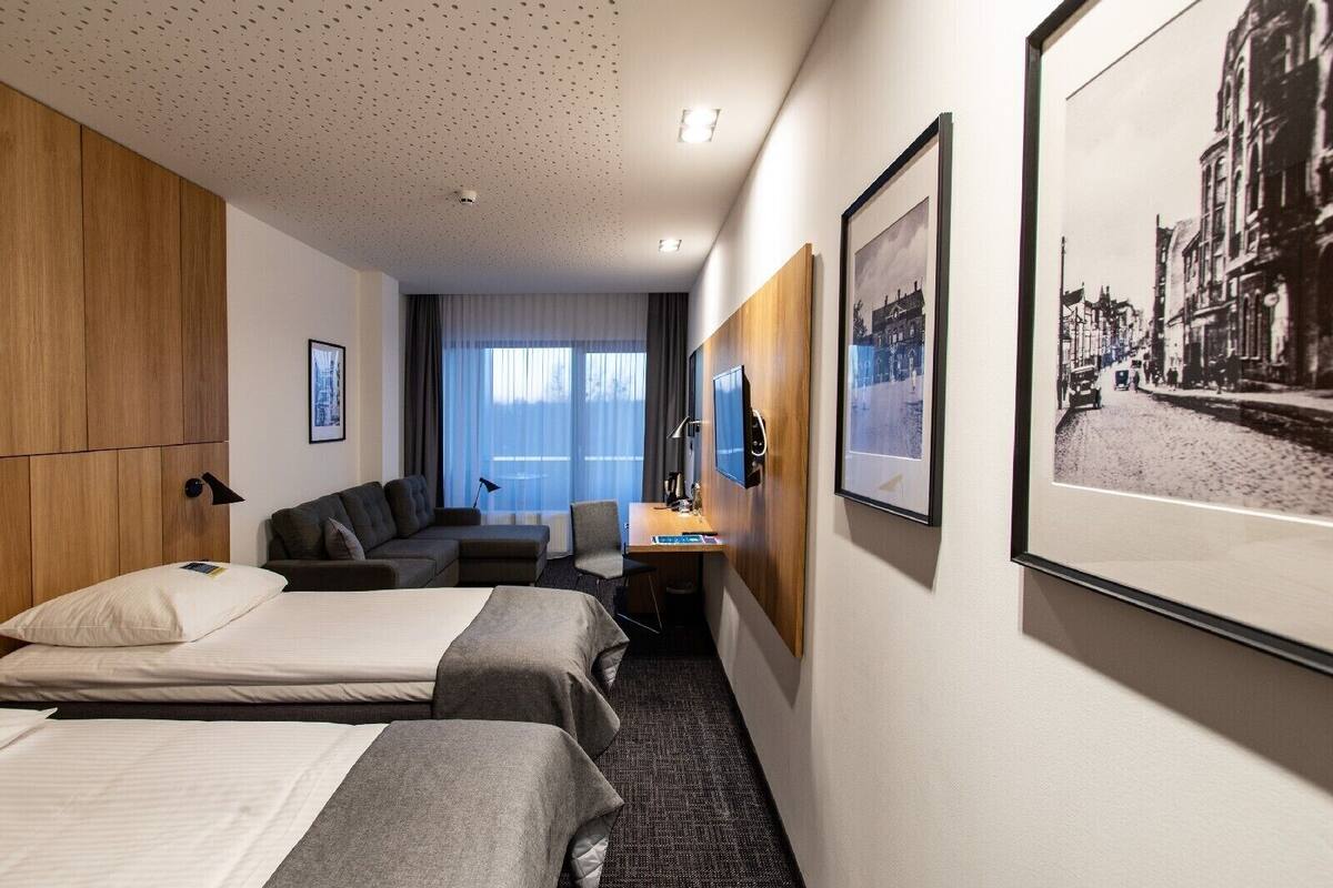 A hotel room with two beds, a sofa, a desk, and a large window.