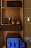 Un minibar con cafetera, tetera y tazas. Abajo, un refrigerador contiene agua embotellada.