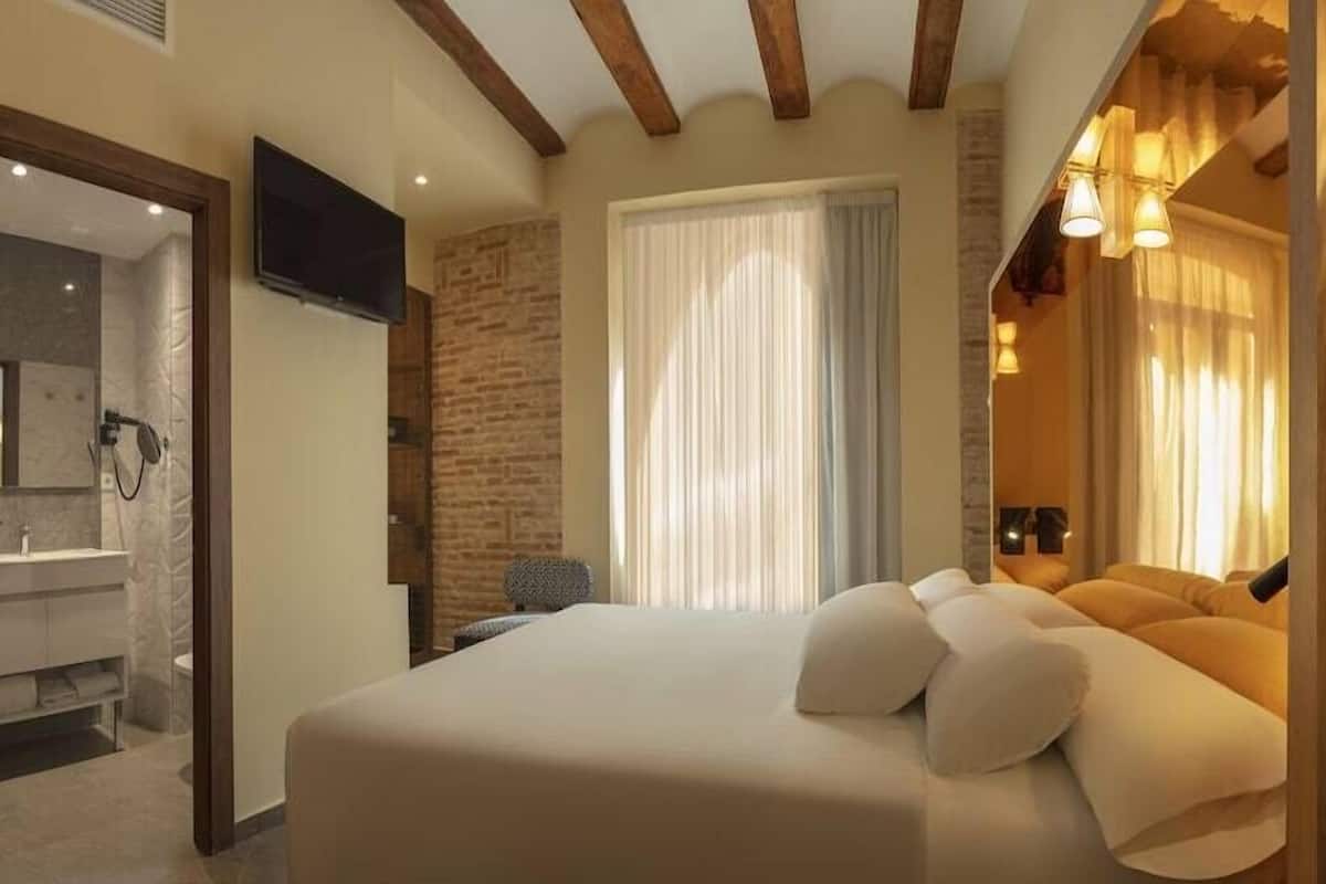 A hotel room with a bed, a TV, a bathroom, and a window with curtains.