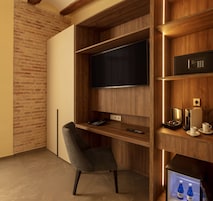 Una habitación moderna con un escritorio de madera, televisión, cafetera y refrigerador.