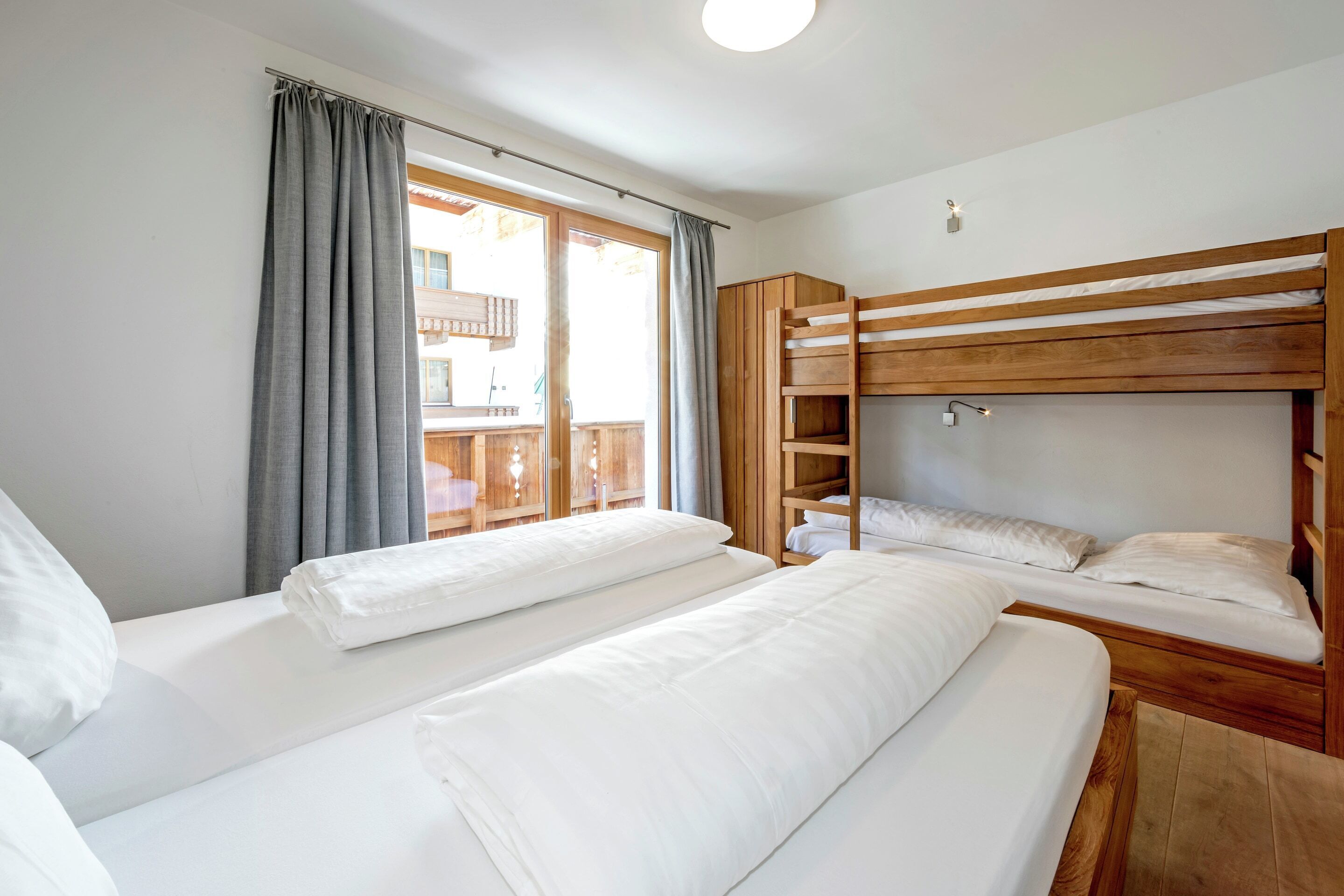 Ein Zimmer mit zwei Betten, darunter ein Holzbettgestell, einem Fenster mit Vorhängen und einem Balkon.