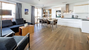 A modern living room with a sofa, coffee table, and dining area with chairs and a table. There is a kitchen with white cabinets and a countertop. - Apartment in Gerlos Near Ski Lift (Gerlos)