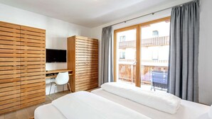 A hotel room with a bed, a desk, a TV, and a balcony with curtains. - Apartment in Gerlos Near Ski Lift (Gerlos)