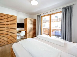 Une chambre d’hôtel avec un lit, un bureau, une télévision et un balcon avec des rideaux.