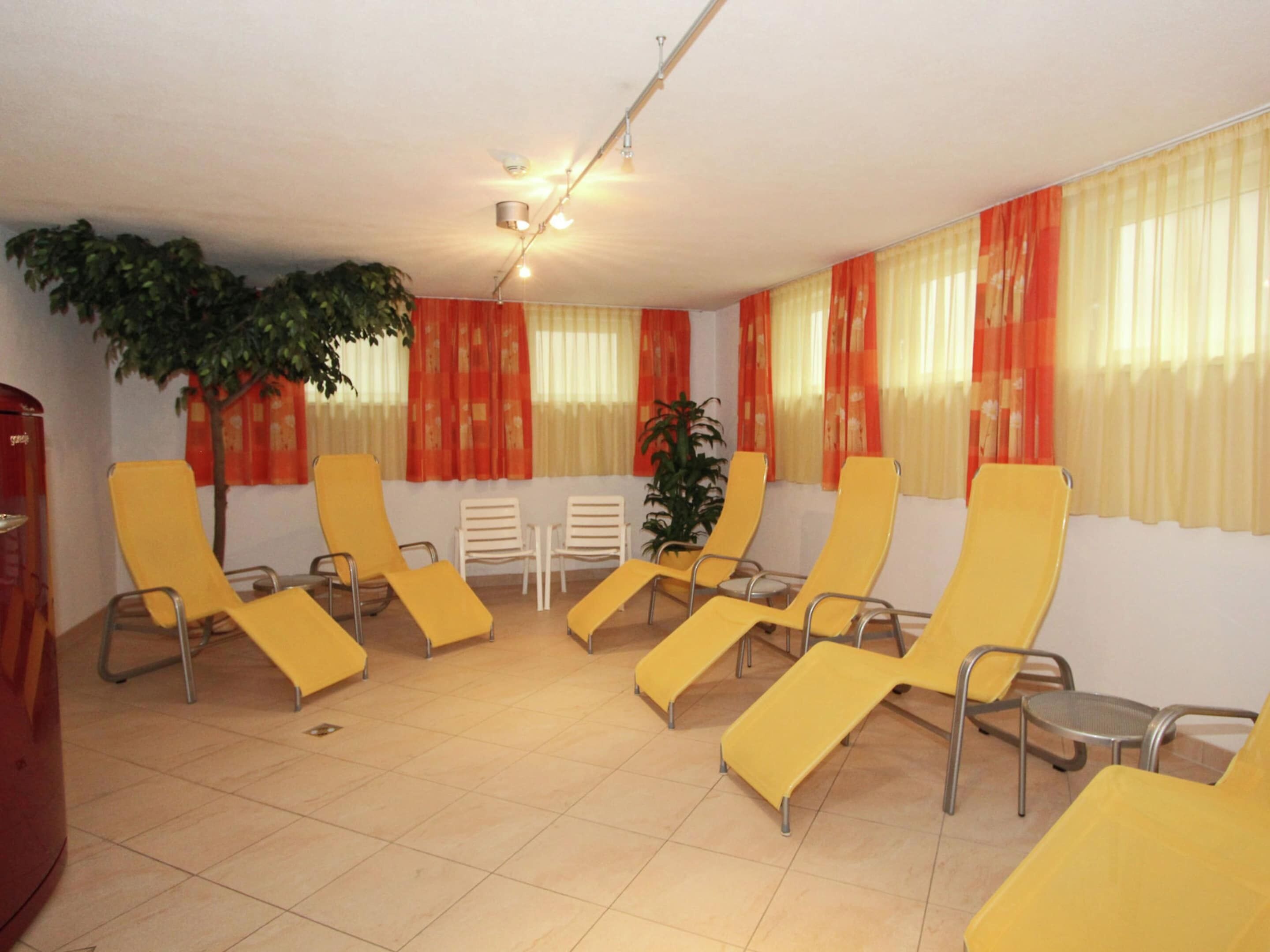 A room with yellow lounge chairs arranged in a semi-circle, a small table, and a potted plant.
