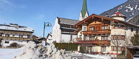 A hotel with a traditional Alpine architectural style, featuring a prominent church steeple and a snow-covered landscape.