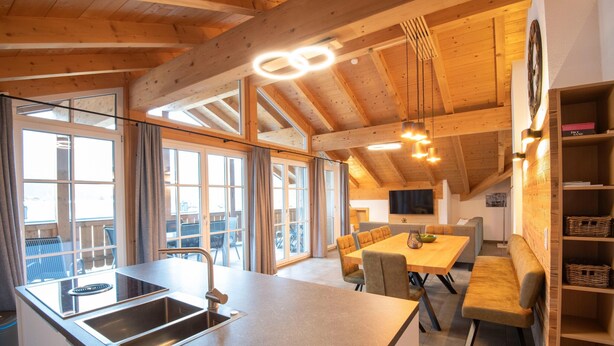 A modern kitchen with a large island, built-in oven, and a dining area with a wooden table and chairs. - Luxury Apartment in Brixen (Brixen im Thale)