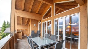 A wooden deck with a glass table and chairs, large windows, and a view of the outdoors. - Luxury Apartment in Brixen (Brixen im Thale)