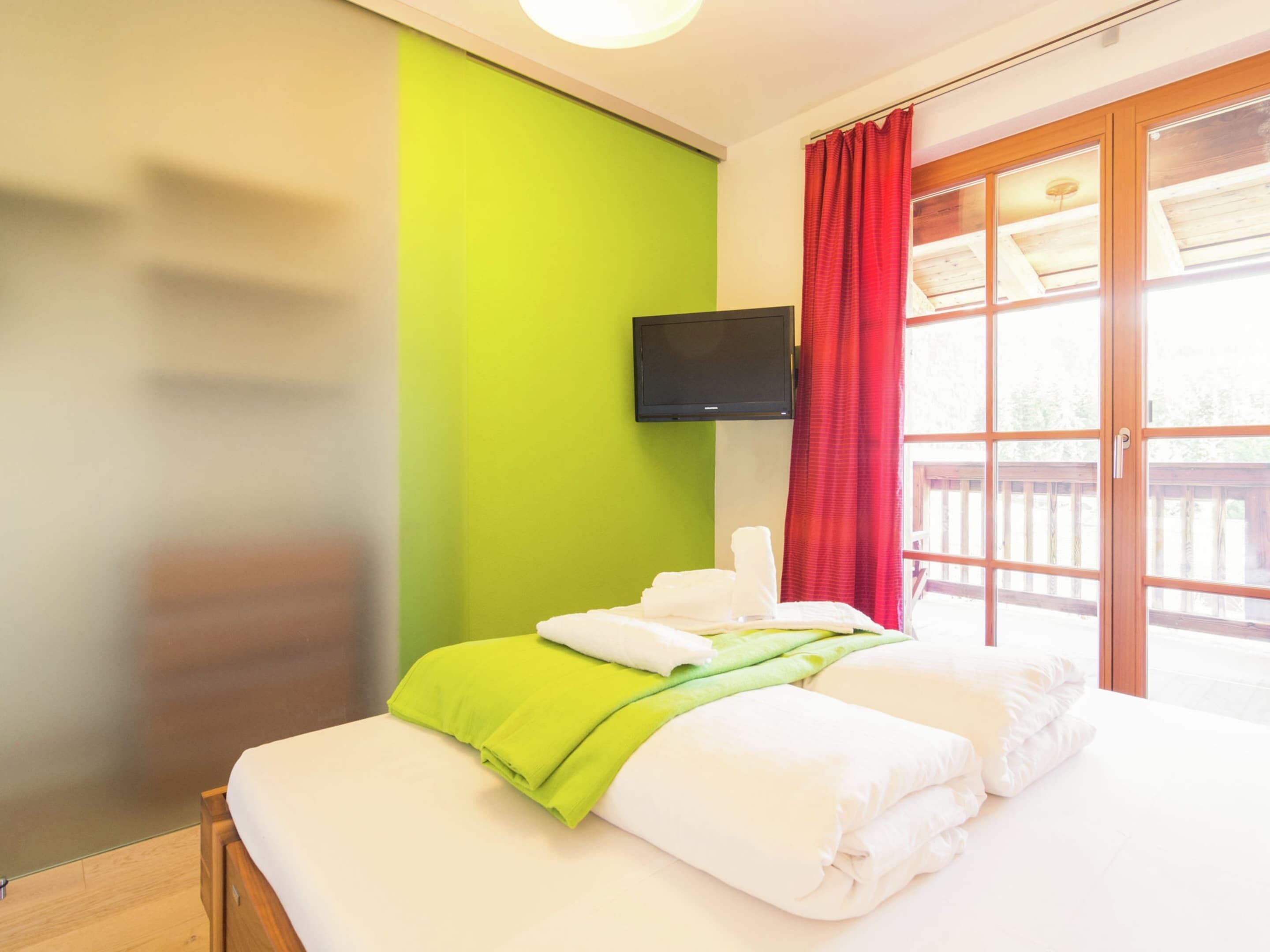 Une chambre d’hôtel avec un lit, un mur vert, des rideaux rouges et un téléviseur fixé au mur.