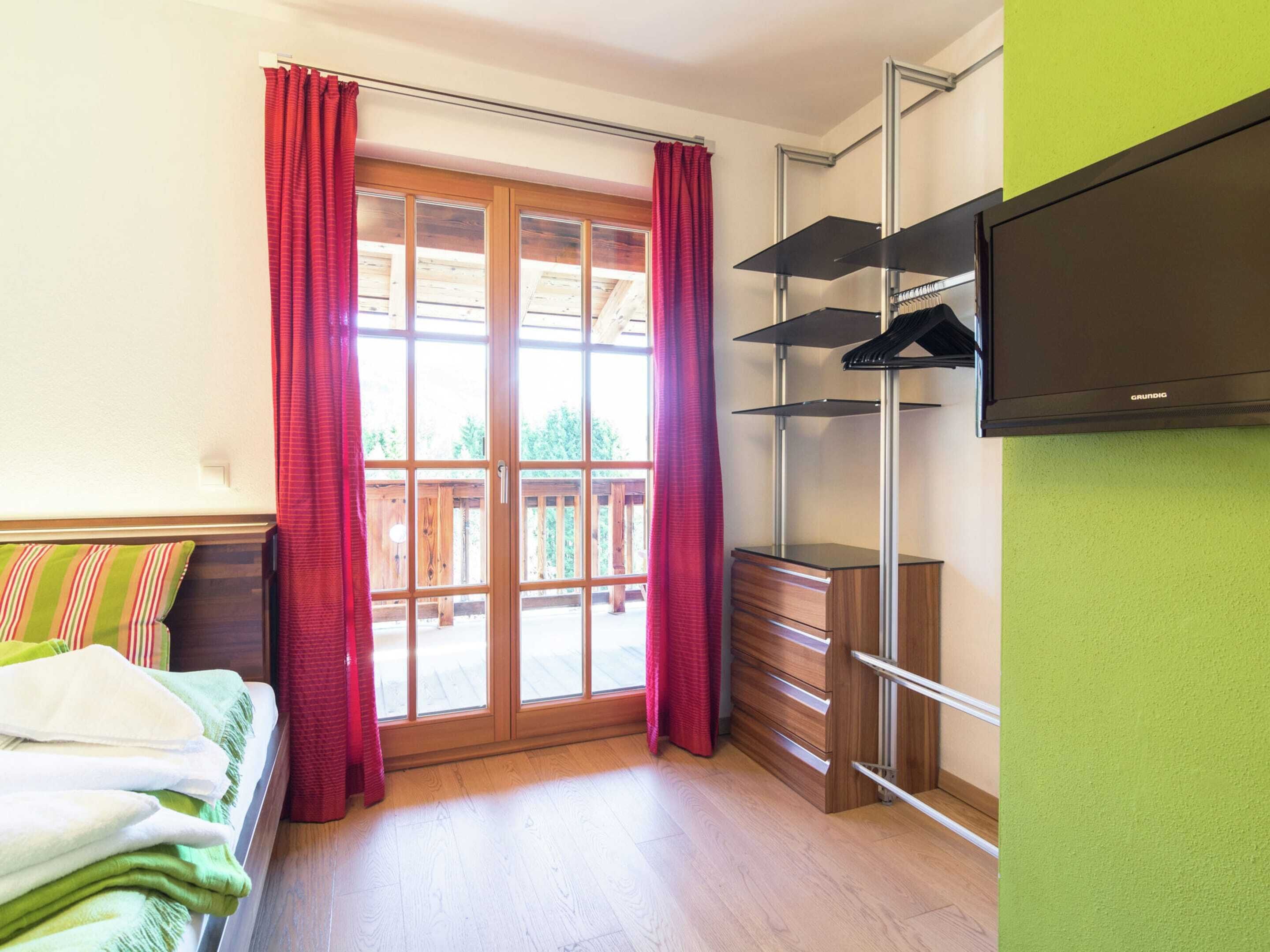 A hotel room with a bed, a wooden dresser, a television mounted on the wall, and a sliding glass door leading to an outdoor patio.