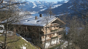 A multi-story wooden chalet with a snow-covered roof, set against a backdrop of snow-capped mountains. - Elite Chalet near Ski Slopes in Westendorf (Westendorf)