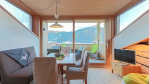 A modern room with a dining table, chairs, a sofa, a TV, and a large window with a mountain view. - Elite Chalet near Ski Slopes in Westendorf (Westendorf)