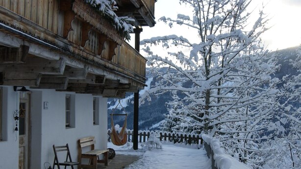 A snow-covered wooden building with a balcony, a hanging hammock, and a stone pathway leading to a snow-covered fence. - Elite Chalet near Ski Slopes in Westendorf (Westendorf)