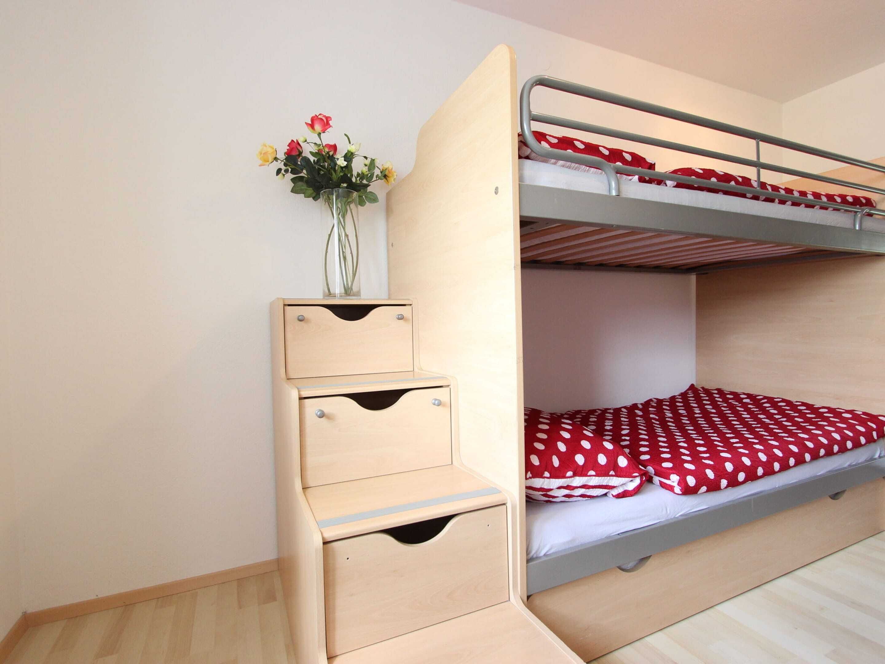 A bunk bed with a lower bunk, a small wooden desk with drawers, and a vase with flowers on the desk.