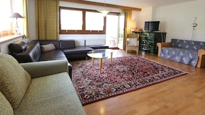 Ein Wohnzimmer mit einer Couch, einem gemusterten Sessel, einem Glastisch und einem roten Teppich.