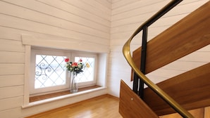 Eine Holztreppe mit Metallgeländer, ein Fenster mit schmiedeeisernen Gitterstäben und eine Vase mit Blumen auf dem Boden.