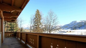 A wooden balcony with a view of snow-covered mountains and trees.