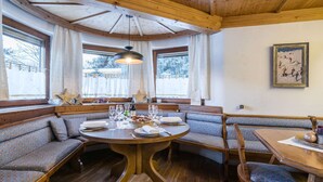 A cozy dining area with a round wooden table, cushioned benches, and a large window with curtains.